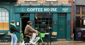 Two Lime riders using an electric scooter and e-bike outside a coffee shop
